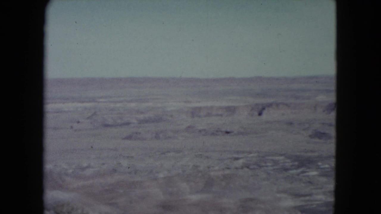 1960 Nevada home-movie frame with a broad arid desert view, low ridges, and faded color in the sky and land.
