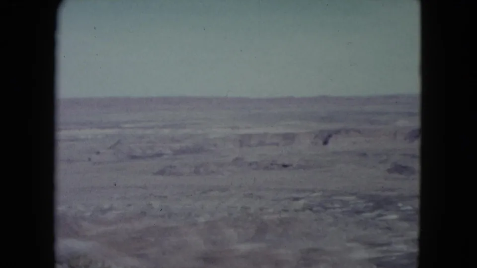 1960 Nevada home-movie frame with a broad arid desert view, low ridges, and faded color in the sky and land.