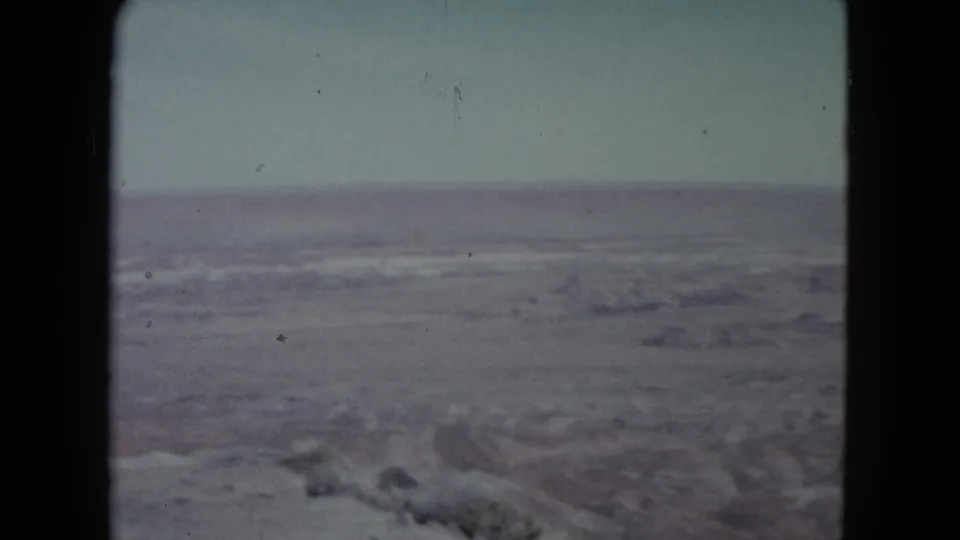 1960 Nevada 8mm view of a dry desert basin with faint ridges and a washed, pale sky.