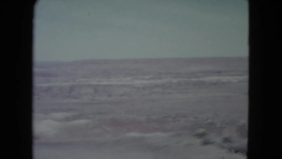 1960 Nevada home-movie frame showing low desert hills, dry open terrain, and pale sky in faded 8mm color.