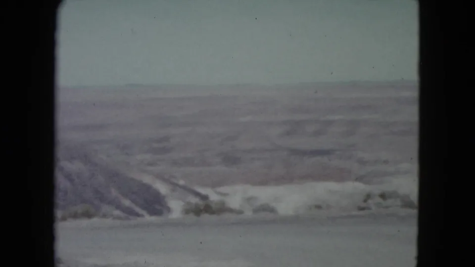 Faded 8mm home-movie frame of Nevada canyon scenery, with a rocky overlook and distant desert formations.