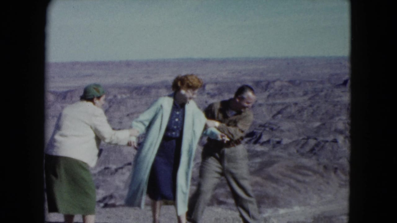 In 1960 Nevada home-movie footage, two women and a man pose playfully near a desert cliff edge with open terrain behind them.