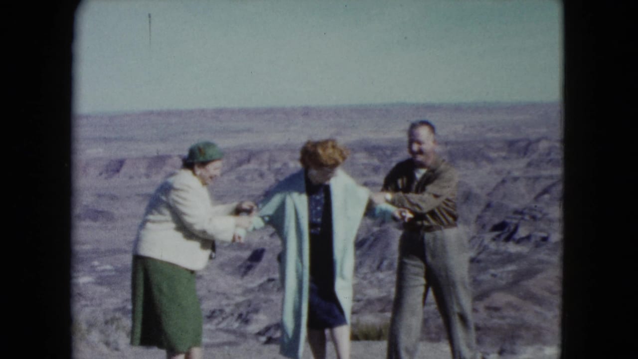 The group continues a playful pose on a Nevada desert cliff edge, with the woman in the blue coat held between the others.