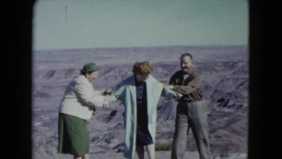 The group continues a playful pose on a Nevada desert cliff edge, with the woman in the blue coat held between the others.