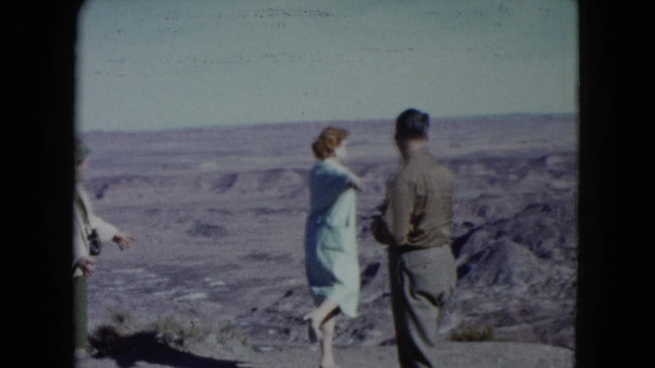 Adults stand at a desert overlook with layered arid terrain in the background.