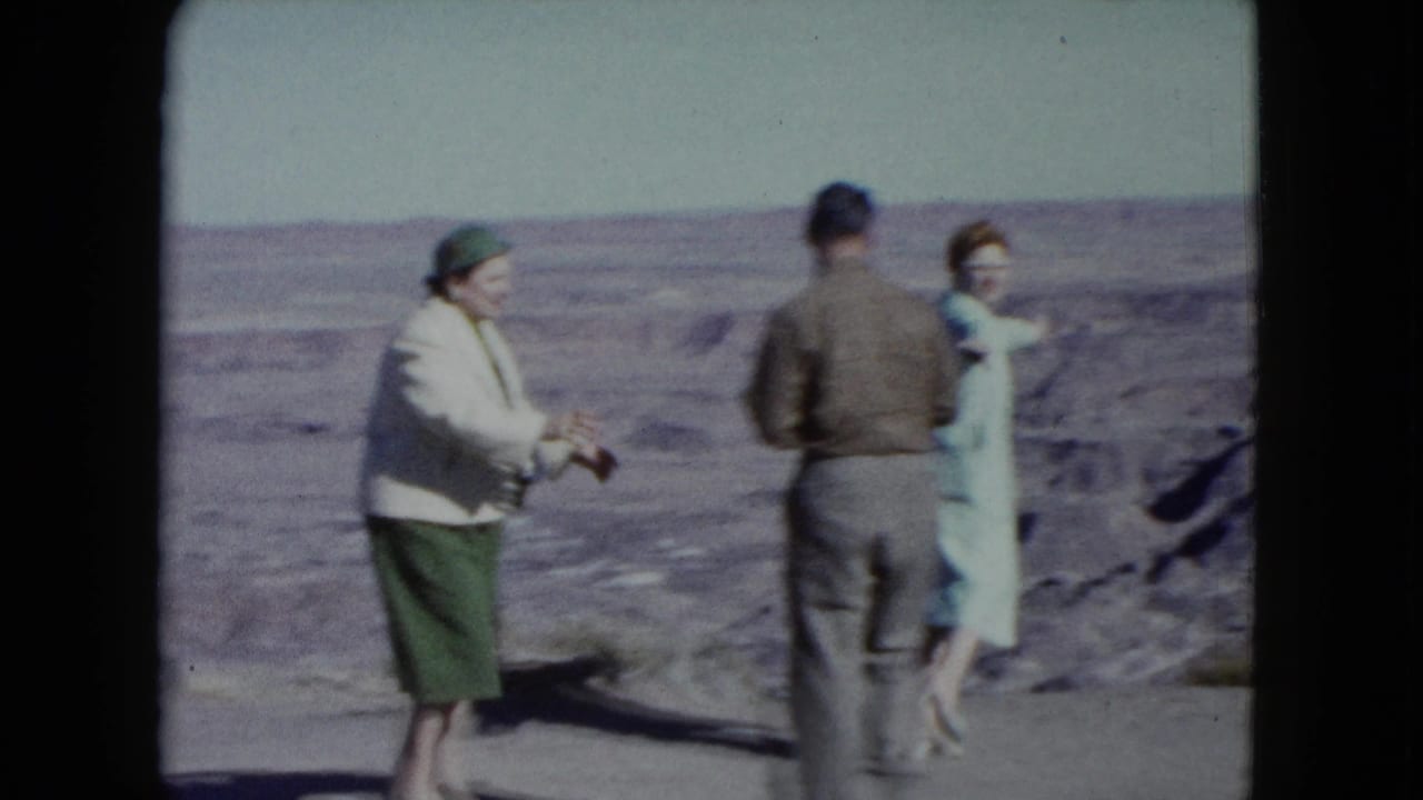 1960 Nevada frame showing three adults in coats and hats at a desert overlook, positioned against a wide arid landscape.