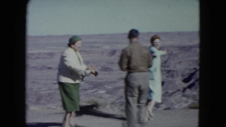 1960 Nevada frame showing three adults in coats and hats at a desert overlook, positioned against a wide arid landscape.