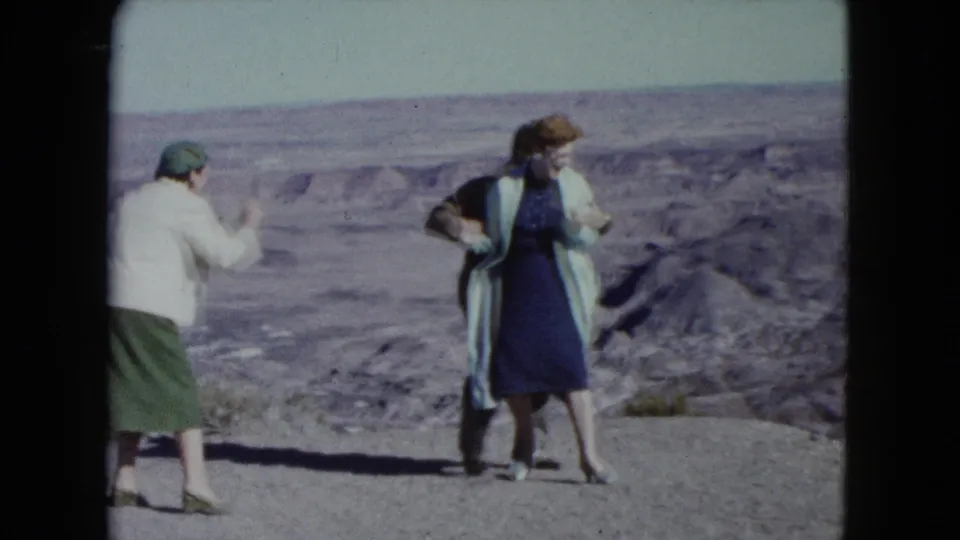 1960 Nevada home-movie frame of two women at a desert viewpoint, with rocky terrain and distant layers behind them.