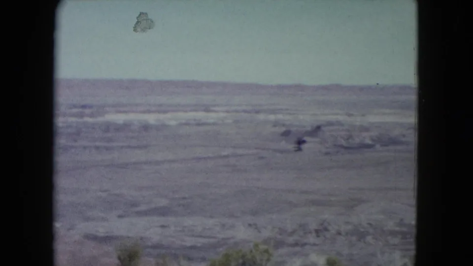 1960 Nevada frame of a broad arid landscape seen from an overlook, with layered desert terrain under a pale sky.