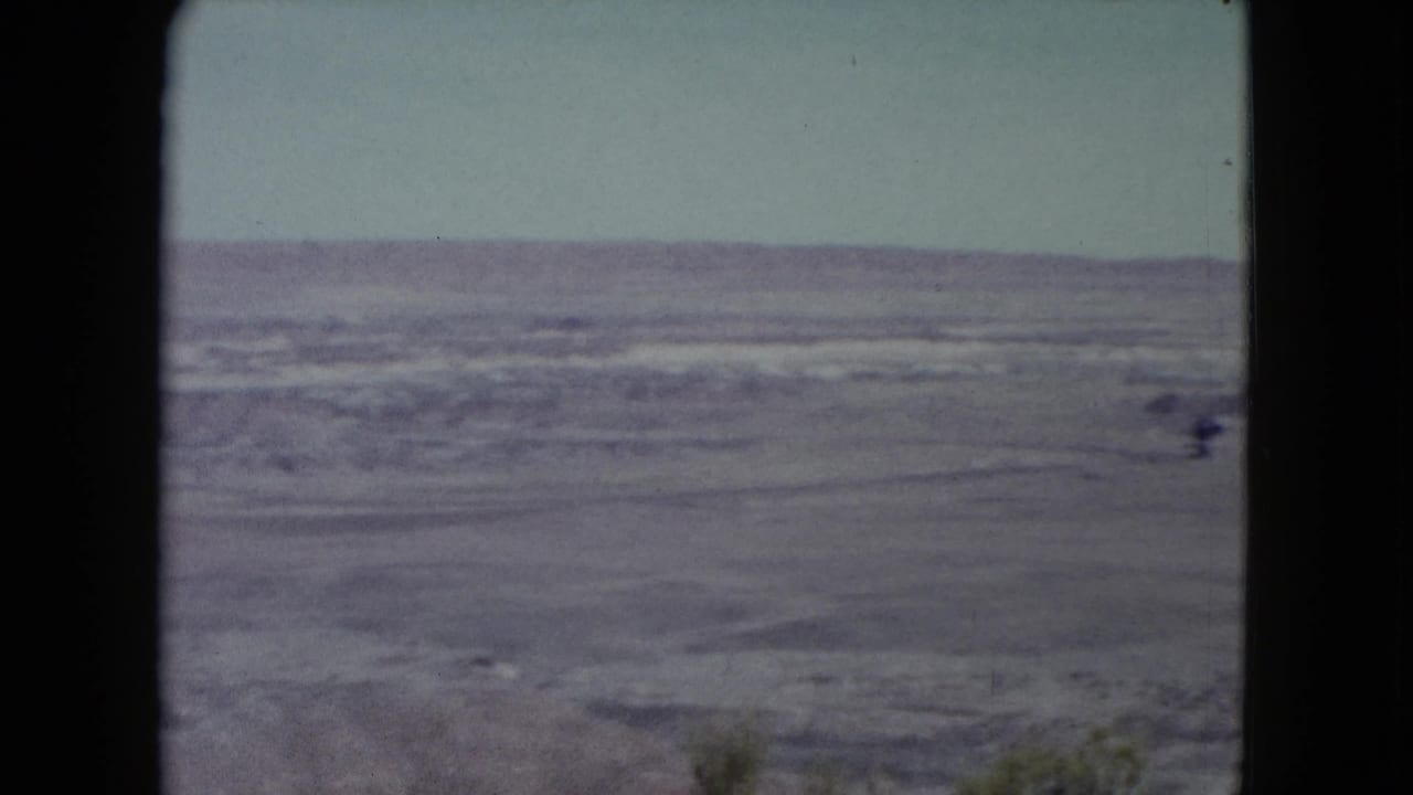 Wide dry desert plain under a pale sky, framed by dark 8mm film edges.