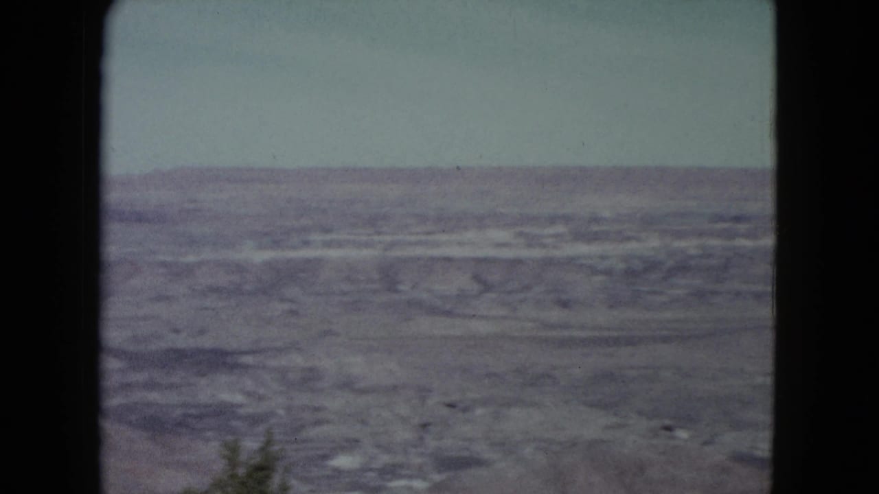 1960 Nevada desert landscape on 8mm, showing textured dry ground beneath a pale sky and visible frame edge.
