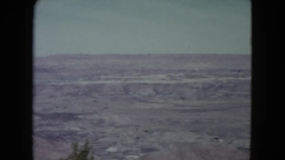 1960 Nevada desert landscape on 8mm, showing textured dry ground beneath a pale sky and visible frame edge.