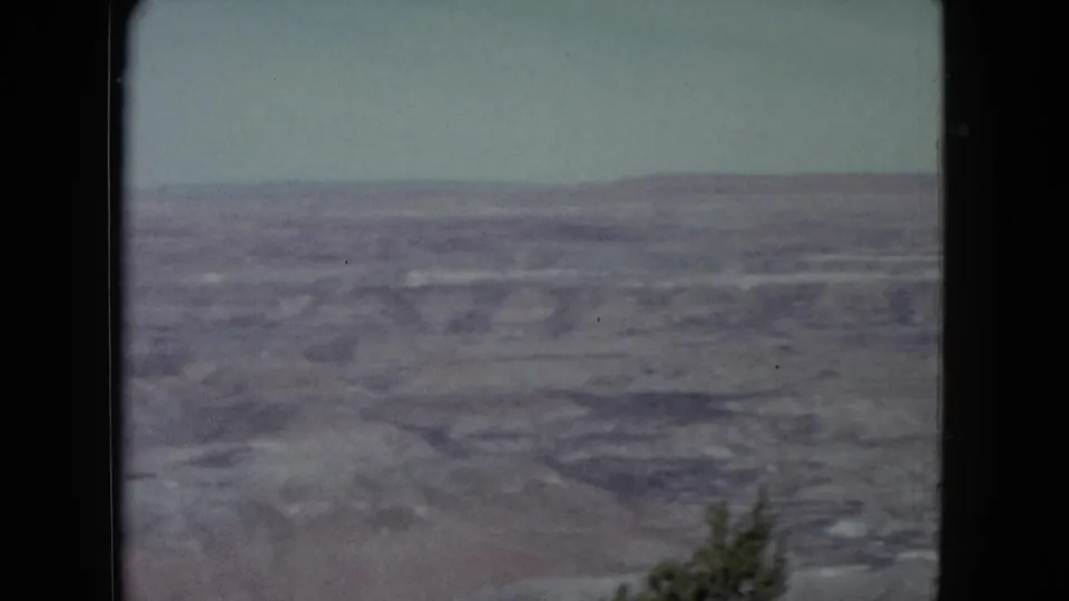1960 Nevada 8mm landscape with sparse shrub at the lower edge and a broad dry plain beyond.