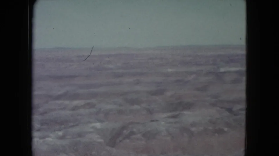 1960 Nevada desert home-movie frame showing open arid ground, distant ridge, pale sky, and light film wear.
