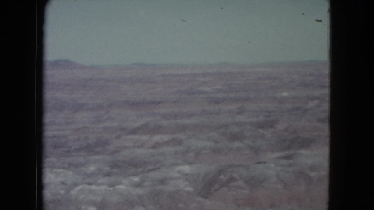 Distant desert plateau under a pale sky with rocky terrain in the foreground.
