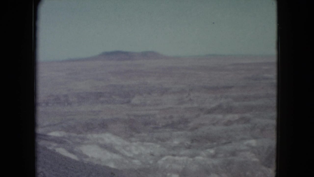 1960 Nevada home-movie frame with a flat-topped plateau beyond muted desert ridges and washes.