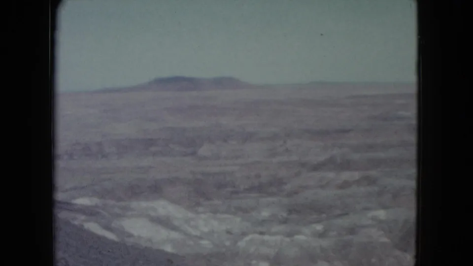 1960 Nevada home-movie frame with a flat-topped plateau beyond muted desert ridges and washes.