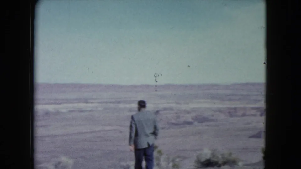 1960 Nevada frame showing a man walking away through barren desert terrain with low hills in the distance.
