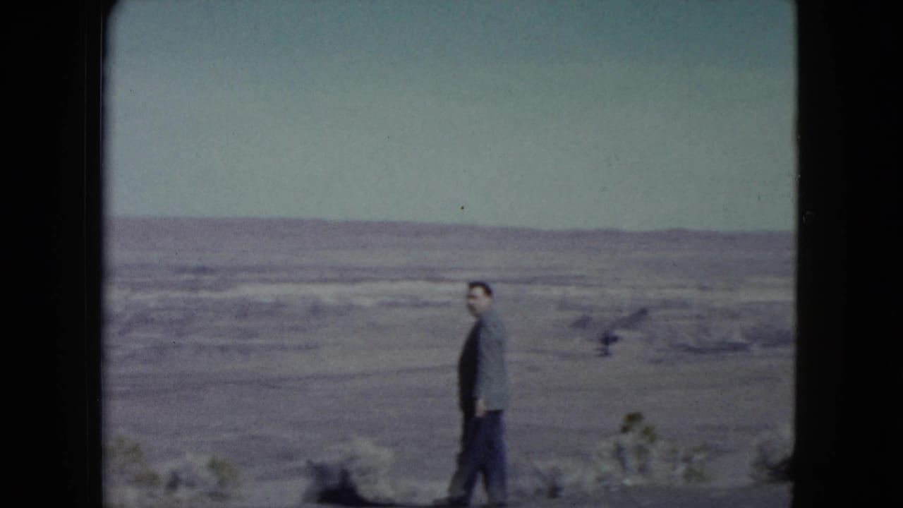 A suited adult man in a Nevada desert setting turns toward the camera, with open arid land and low hills behind him.