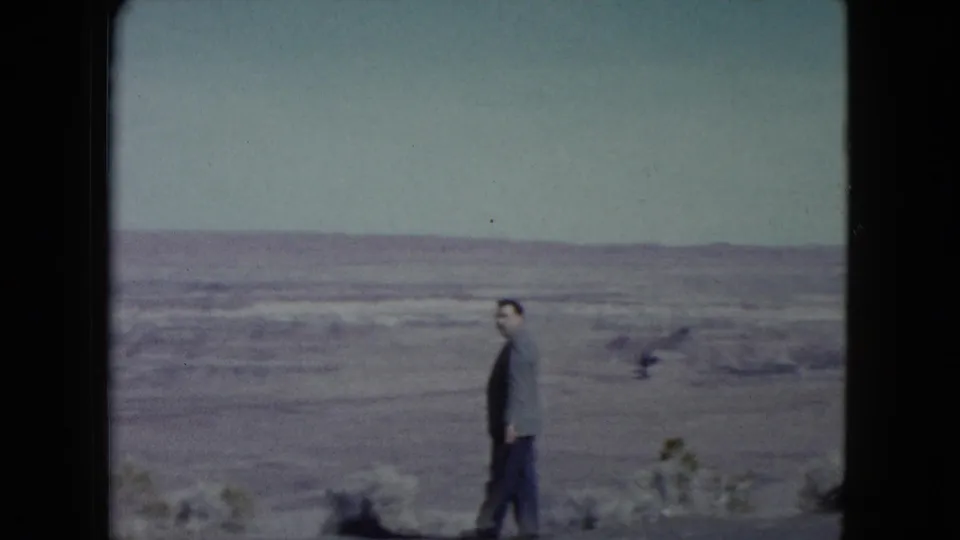 A suited adult man in a Nevada desert setting turns toward the camera, with open arid land and low hills behind him.