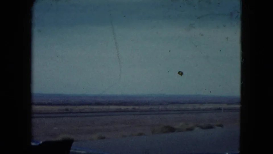 A wide 8mm view of the Nevada desert shows flat arid ground, low distant hills, and a pale sky with no person visible in this frame.