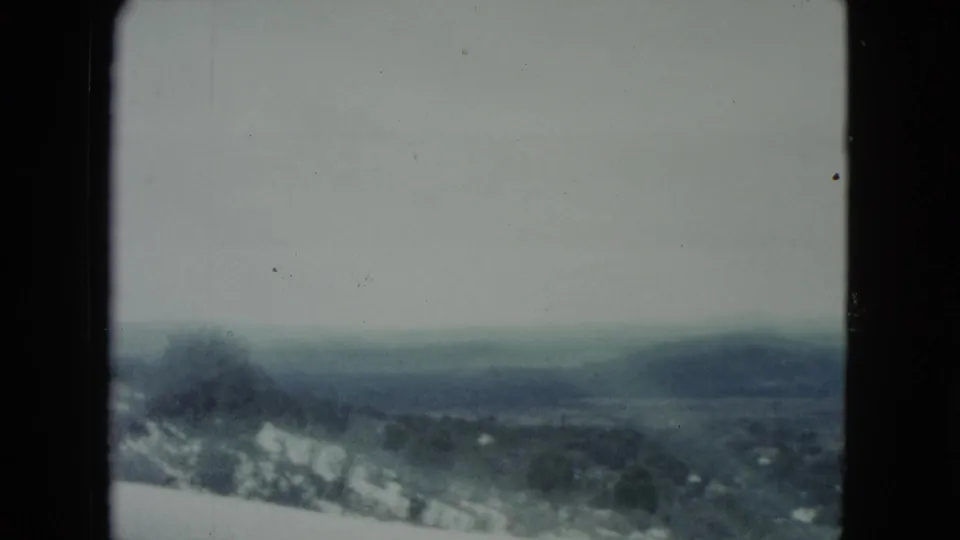 Muted 8mm view of Nevada hills and pale ground patches, partially framed by a dark car-window edge.