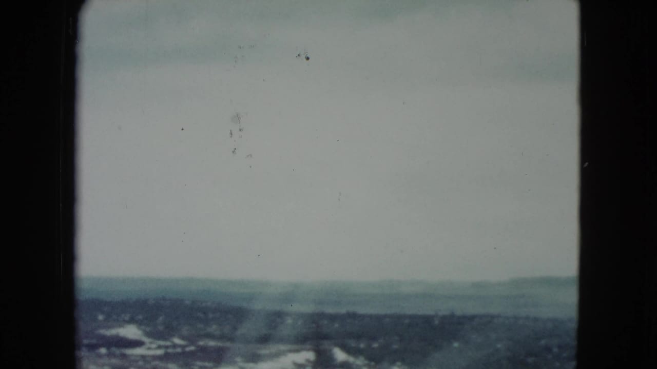 Soft 8mm view of distant desert hills beneath a pale sky, seen across a dark window or film edge.