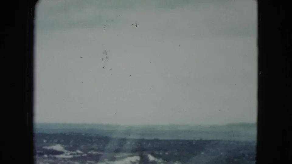 1960 Nevada 8mm frame showing a hazy desert horizon, low hills, and pale sky from a moving travel viewpoint.