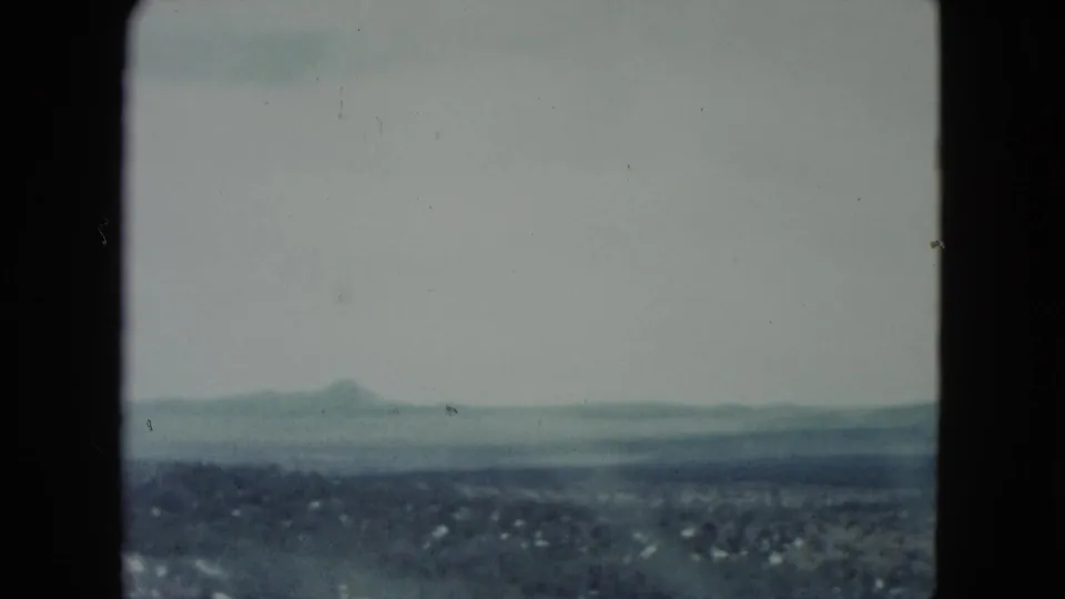 1960 Nevada 8mm view of a broad desert basin and distant low mountains under a washed pale sky.