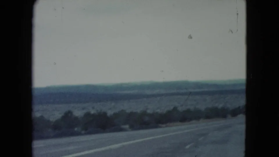 1960 Nevada road-travel frame showing pavement, roadside brush, distant desert ridges, and faded 8mm color.