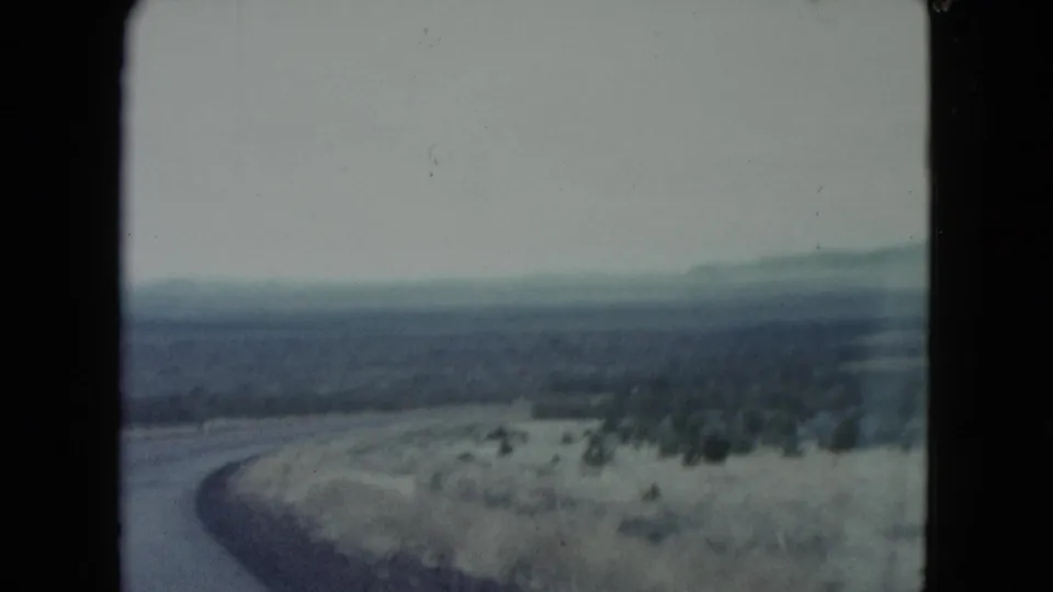 Soft 8mm frame from Nevada showing the road curving out of view beside pale scrubland and low hills on the horizon.
