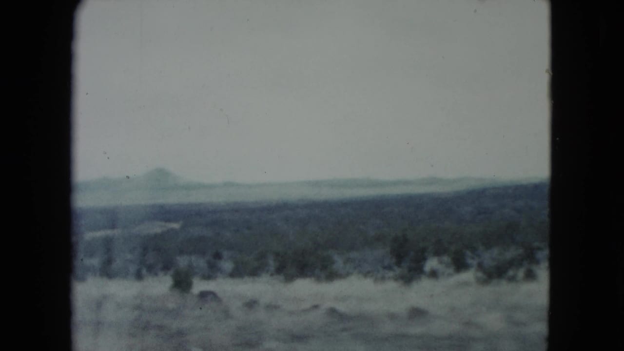 Wide arid landscape with low vegetation and faint mountains beyond the horizon.