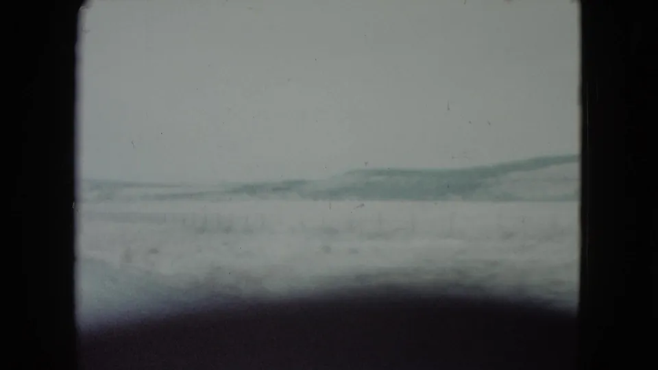 1960 Nevada home-movie frame showing a snowy plain, distant blue-gray hills, and dark gate framing.