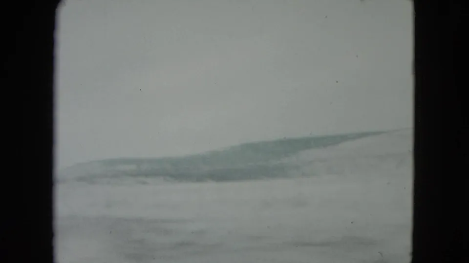 Soft 8mm frame from Nevada shows pale desert ground and distant hills passing by from a moving car.