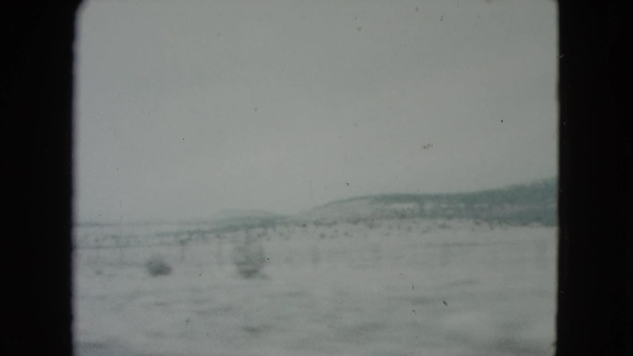 Desert plain and distant low hills seen through a moving vehicle frame.