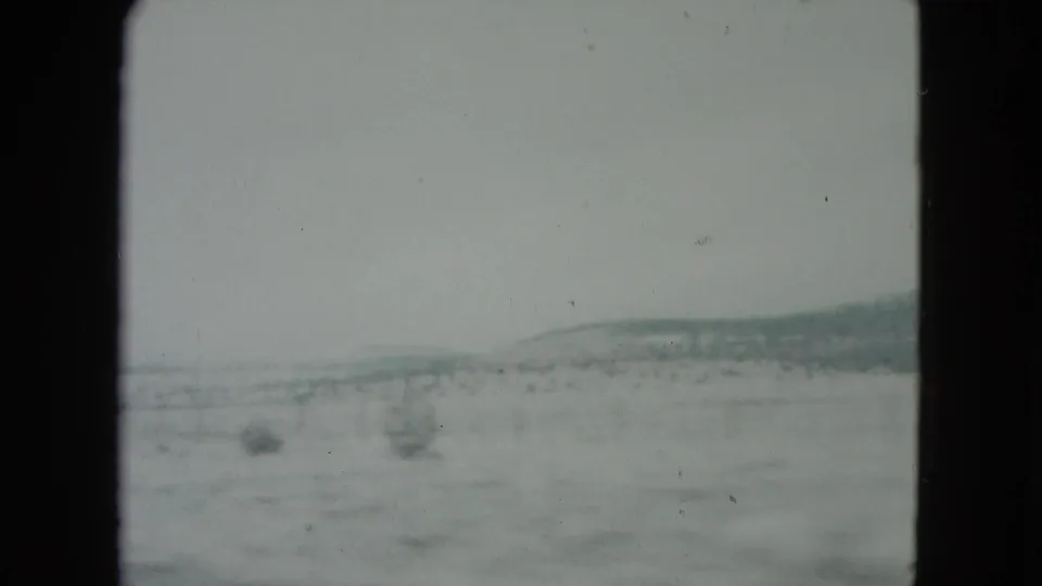 Nevada desert landscape in 1960 home-movie footage, with sparse shrubs and low hills beyond the roadside.