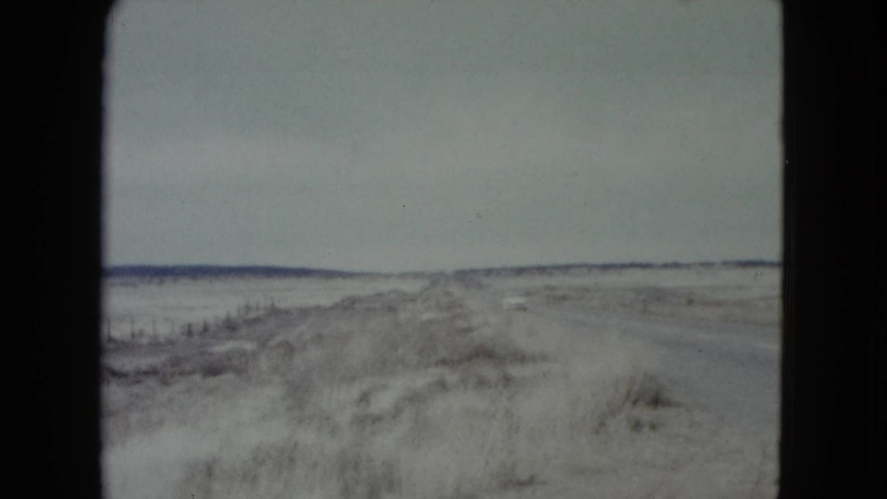 Empty rural road running through sandy brush under a pale sky.