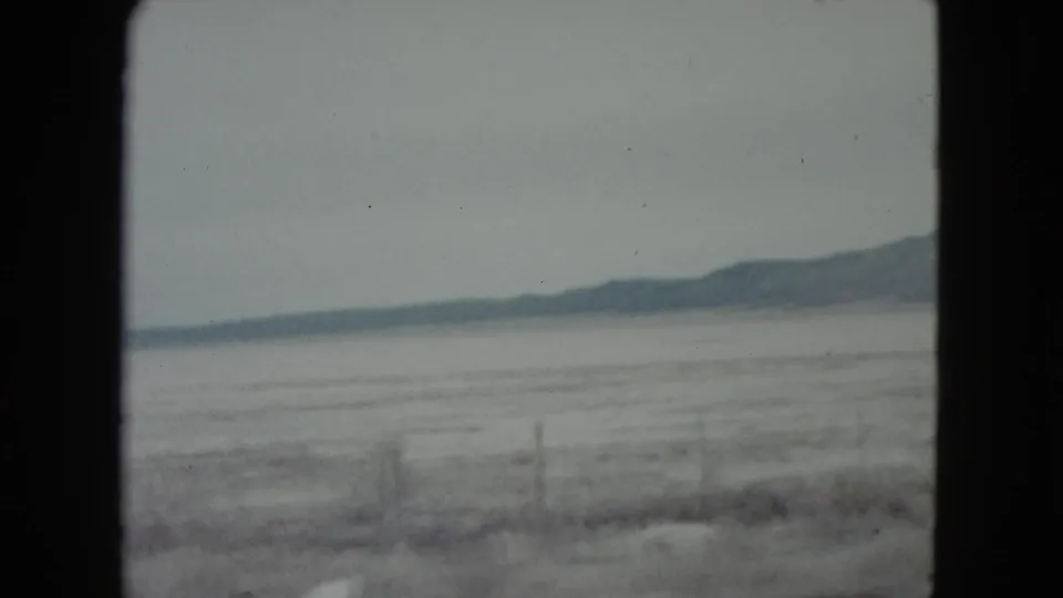 Hazy 1960 Nevada landscape frame with an open frozen plain, low mountain ridge, faint fence posts, and visible 8mm gate borders.