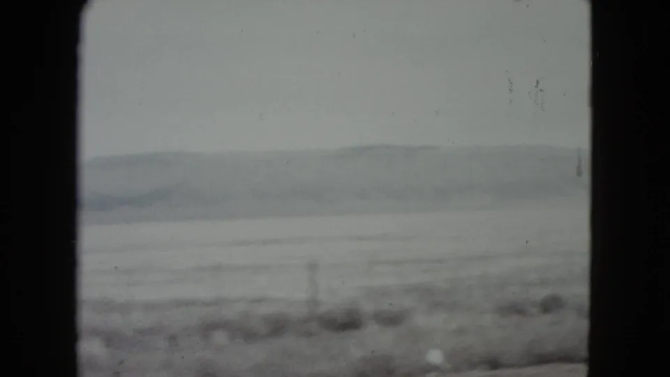 Final 1960 Nevada frame showing a soft, foggy plain, faint distant mountains, scrub vegetation, and a few fence posts near the foreground.