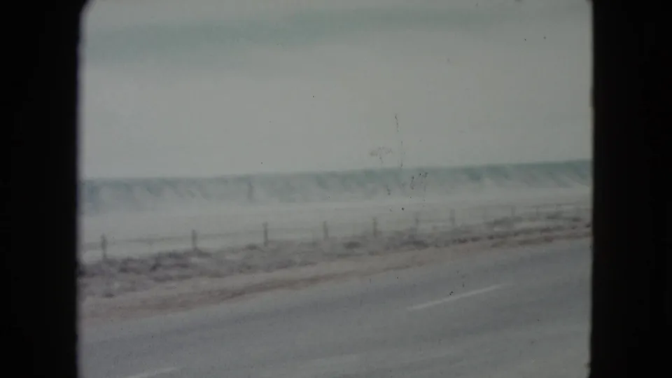 1960 Nevada home-movie view of a paved road beside snow-dusted open ground, fence posts, and low hills.