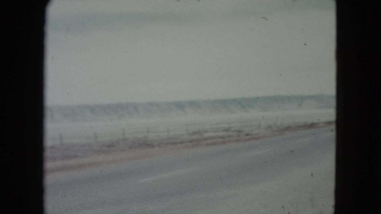Hazy desert highway seen from a moving vehicle with low hills in the distance.