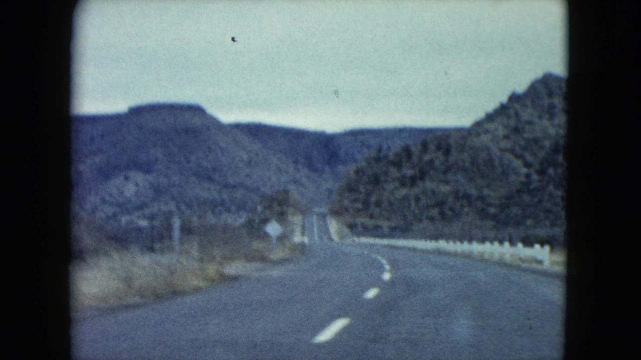 Two-lane desert road curving between rocky hills under a muted sky.