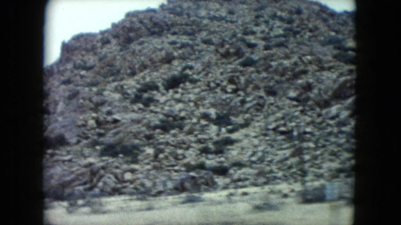 1960 Nevada 8mm frame showing a rocky desert slope with scattered vegetation and soft, faded color.