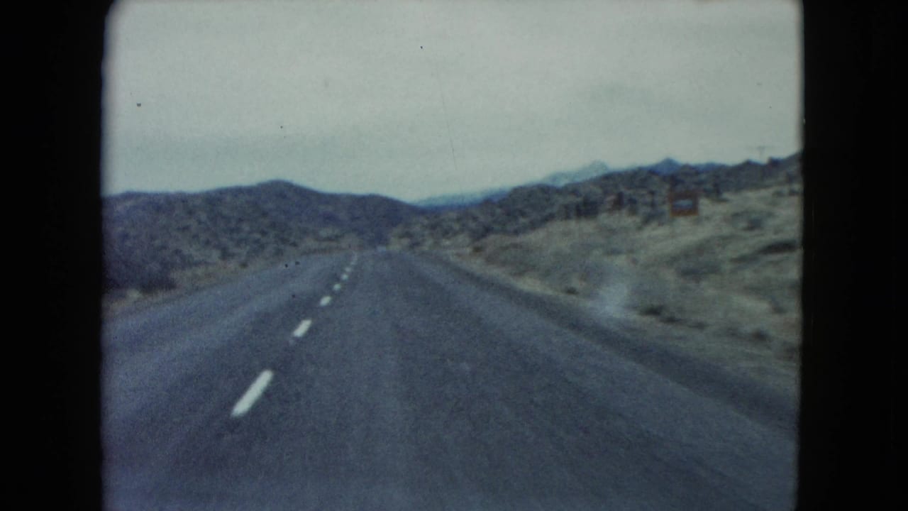 Two-lane desert highway running toward low hills under an overcast sky.
