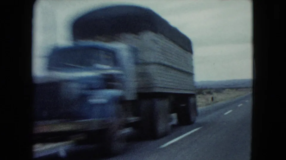 A motion-blurred older truck passes close to the camera on a Nevada desert highway in 1960 home-movie footage.