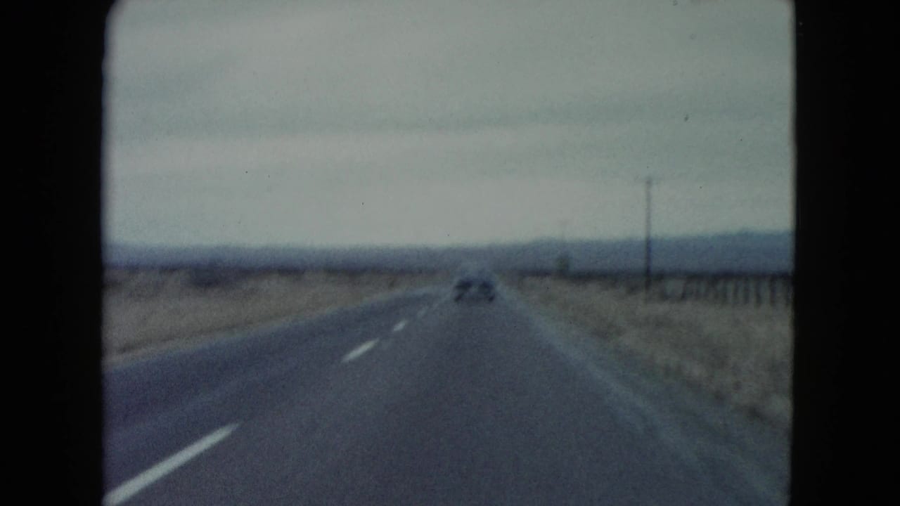 1960 Nevada home-movie frame showing a car ahead on a two-lane desert highway under an overcast sky.