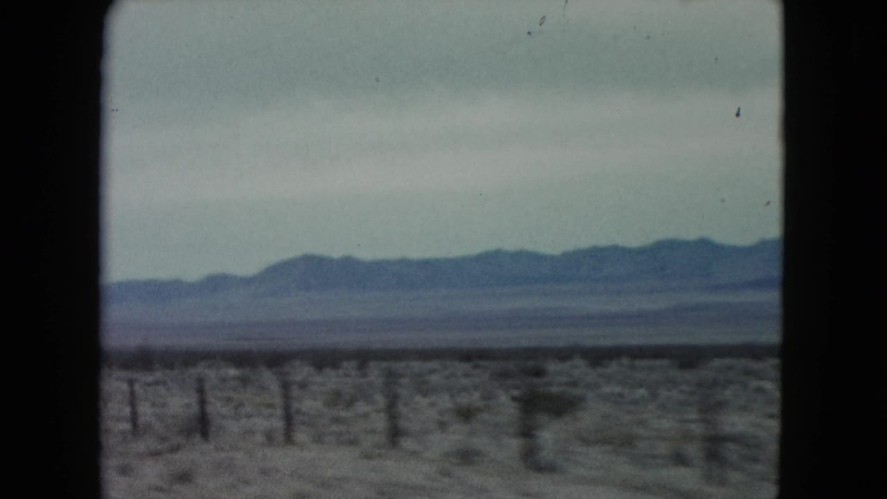 Open desert plain with a fence line and blue-gray mountains in the distance.