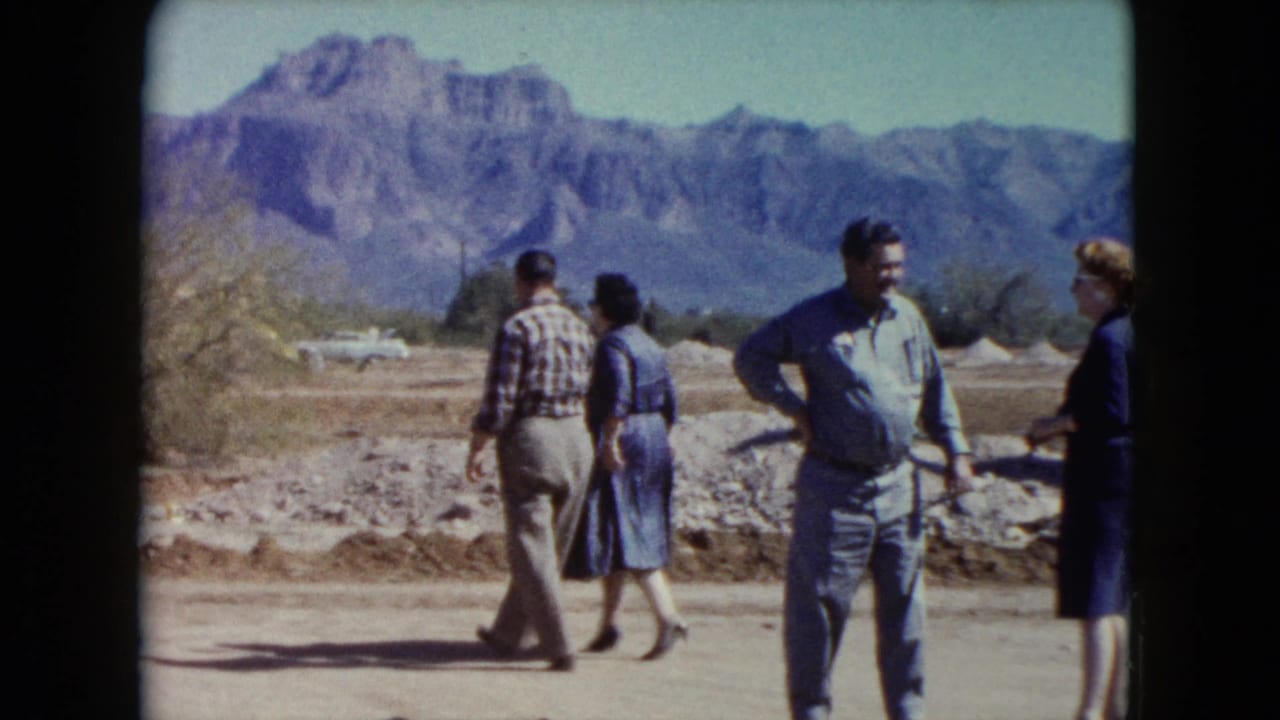 Four adults stand and walk on a dirt path with desert mountains in the background.