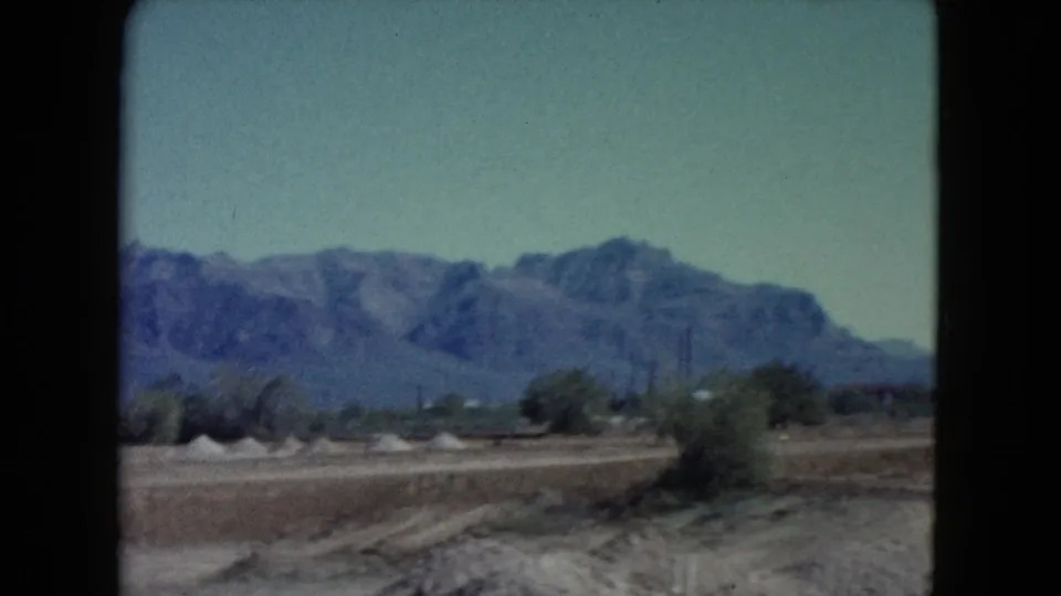 1960 8mm Nevada desert frame with broad mountain backdrop, low vegetation, open ground, and faded color.