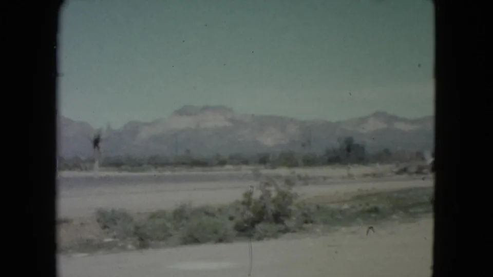 A soft 8mm view of Nevada roadside terrain shows low scrub, a road and hazy mountains under a pale sky.